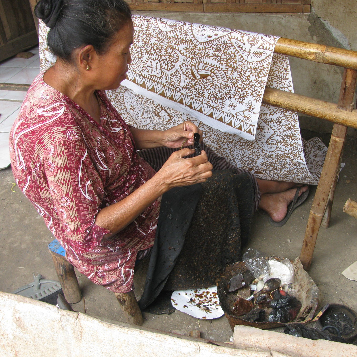 An indonesian woman uses a batik wax pen to draw patterns on primissima fabric.