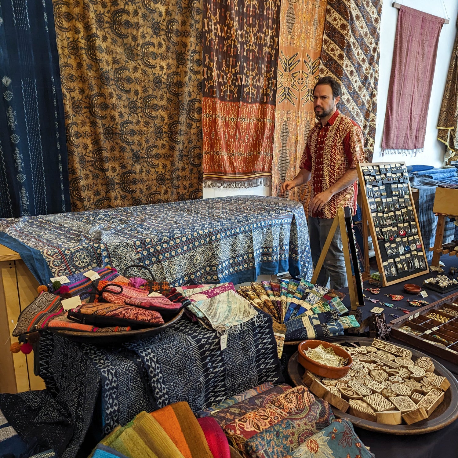 Handmade Asian textiles at a market in the UK. Batik, ikat and handwoven wall hangings decorate a stall.