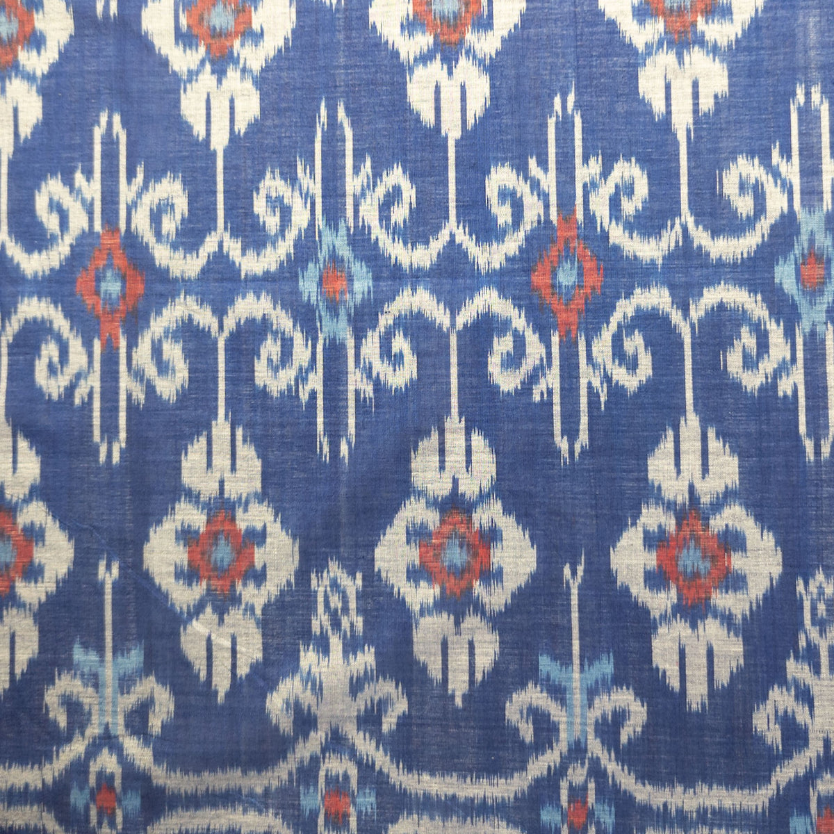 A close-up of a blue woven ikat fabric with a repeating ikat pattern in off-white, light blue, and red.