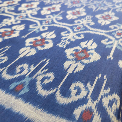 A close-up of a blue fabric with a traditional ikat floral pattern in cream, light blue, and red.