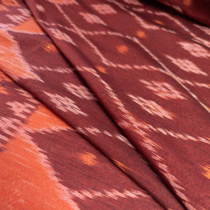 A close-up of folded fabric with an ikat pattern in deep burgundy, rust orange, and light pink, showing the textile's texture and weave.