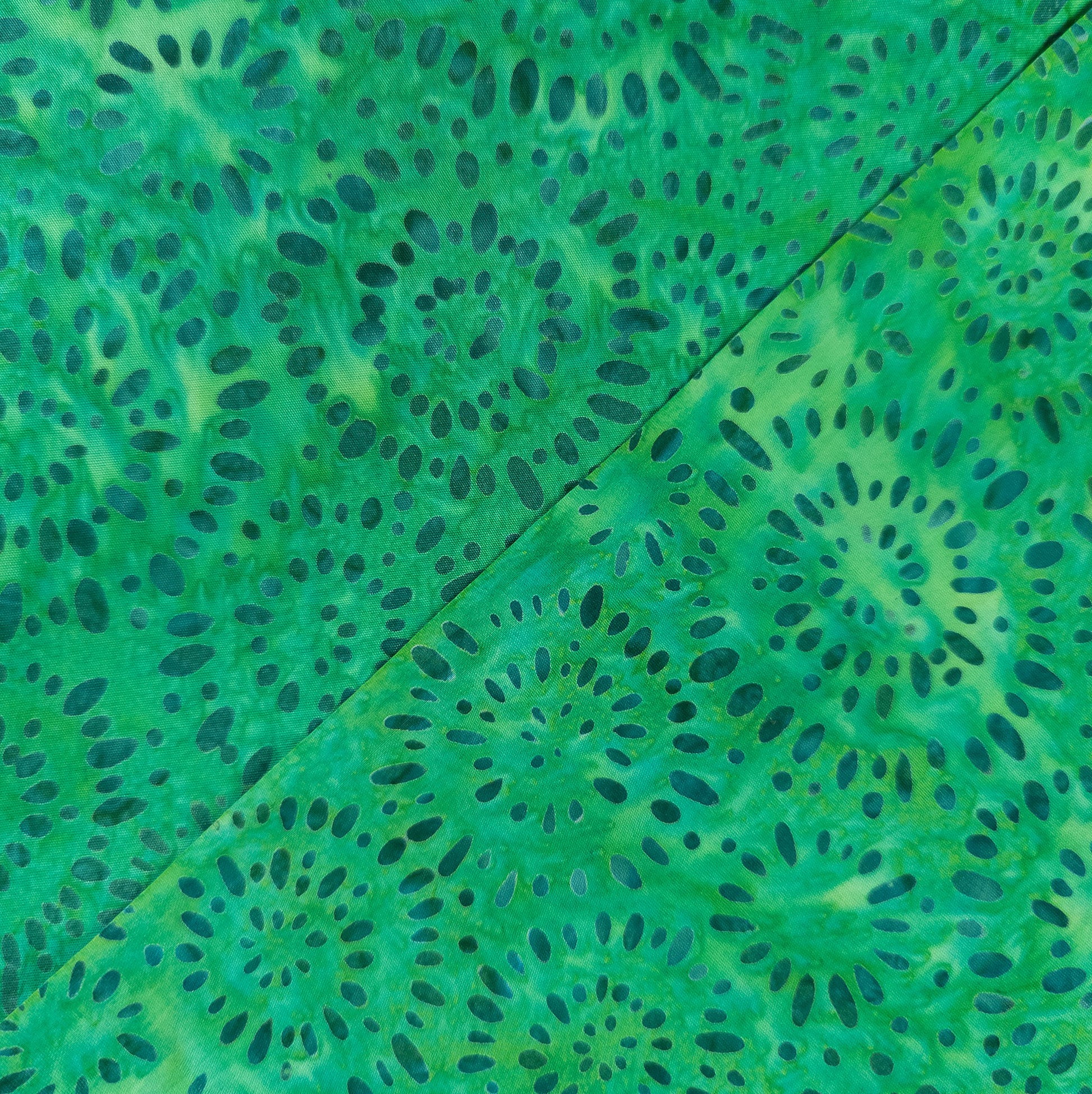 hand printed batik fabric with a teal firework pattern on a bright green cotton background