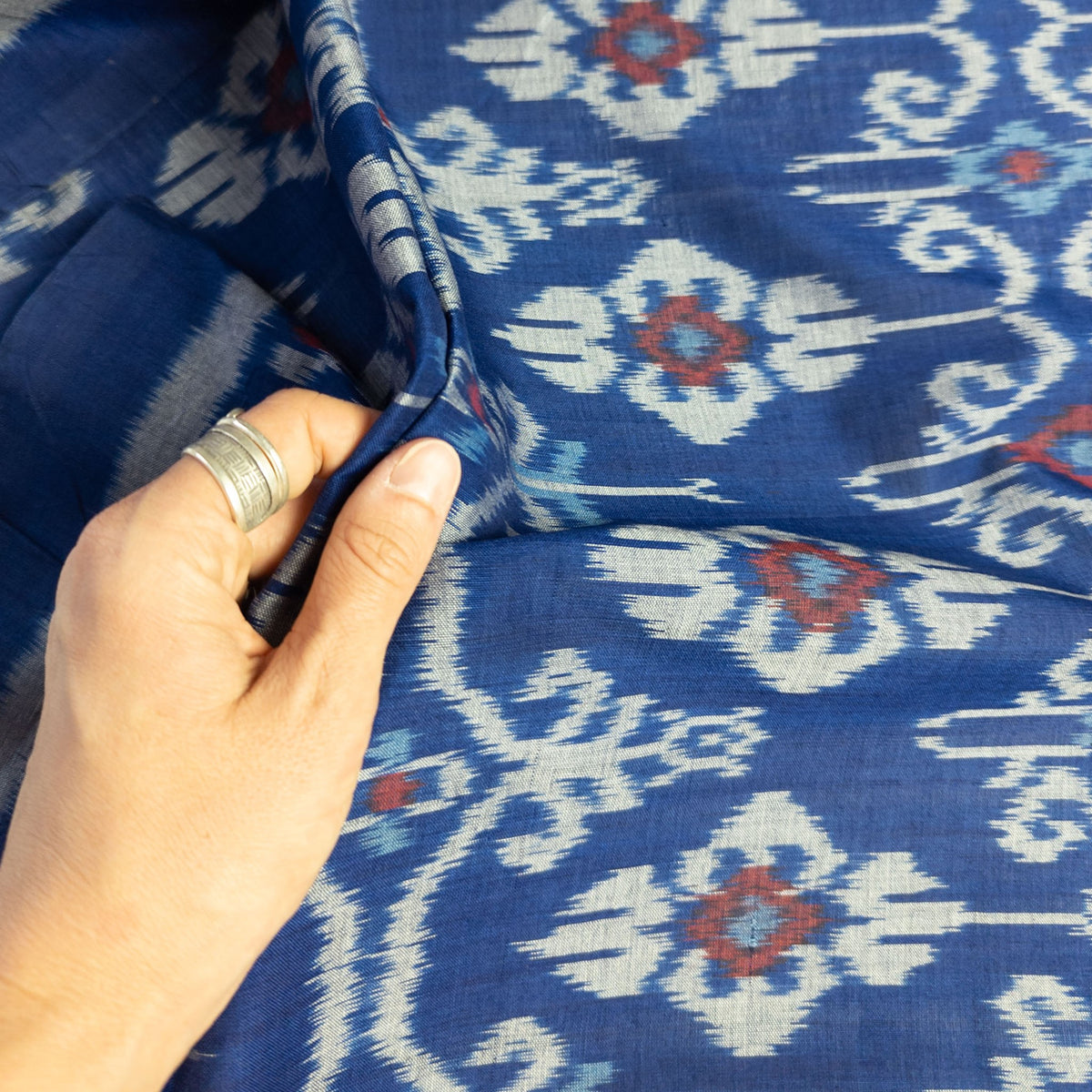 A close-up of a hand holding up a piece of blue patterned fabric with white and red Indonesian ikat motifs.
