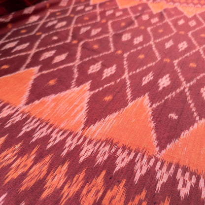 A close-up of patterned fabric with a deep burgundy base, bright orange geometric triangles, and white ikat-style diamond and zigzag motifs.