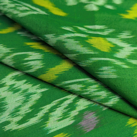 A close-up of folded green ikat fabric with traditional woven pattern in white and yellow, showing the woven texture and color distribution.