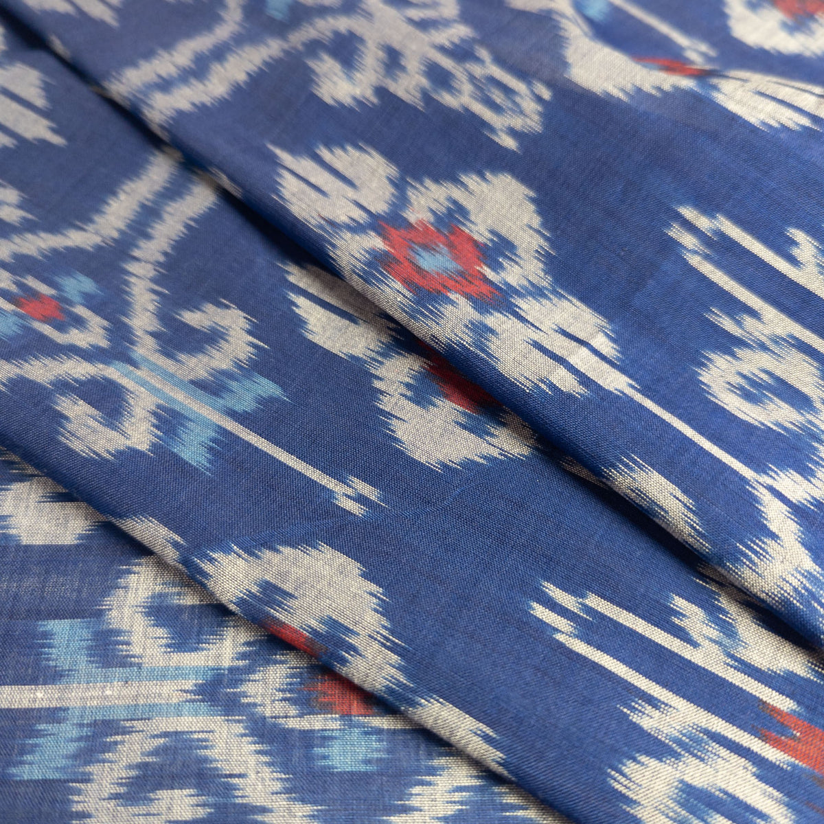 A close-up of folded blue patterned fabric with a traditional Indonesian ikat design in cream, light blue, and red.