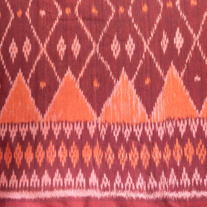 A close-up of a patterned fabric with a deep burgundy background, featuring orange and white ikat-style diamond and triangle motifs.