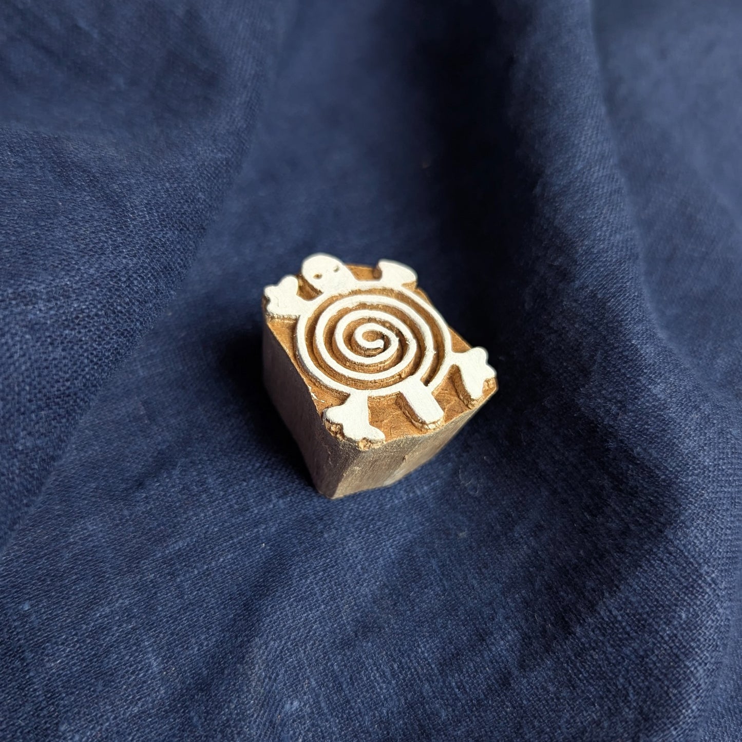 A carved wooden printing block with a spiral shell turtle design.