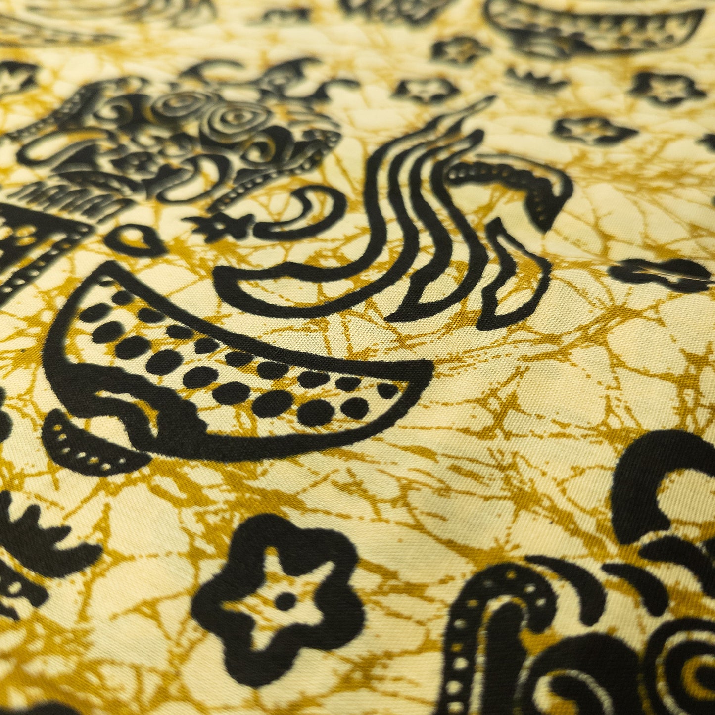 Close up of cotton batik sarong from Bali in a pale yellow colour with black crackle batik overprinted design